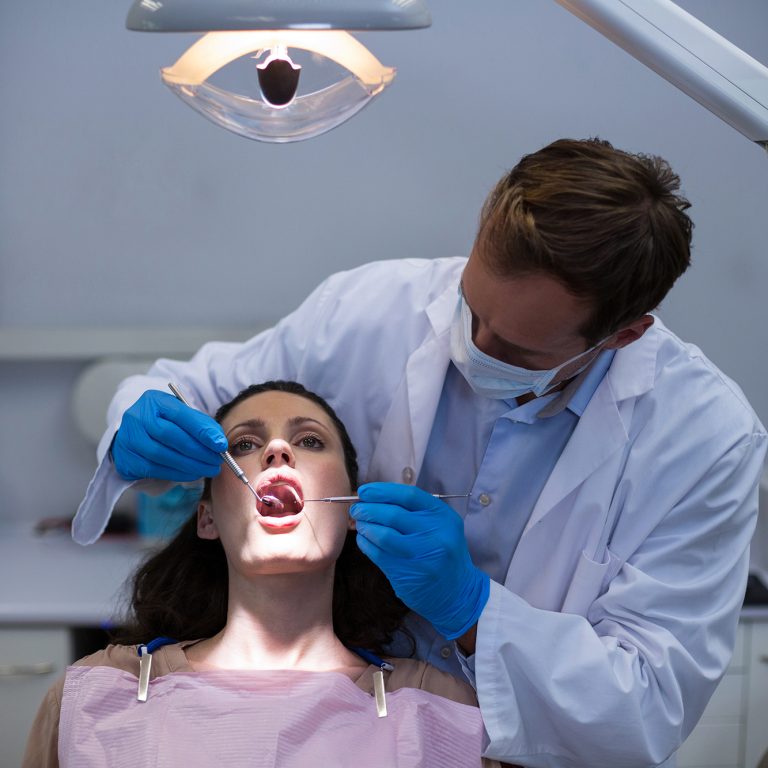 Dentist examining a female patient with tools at dental clinic