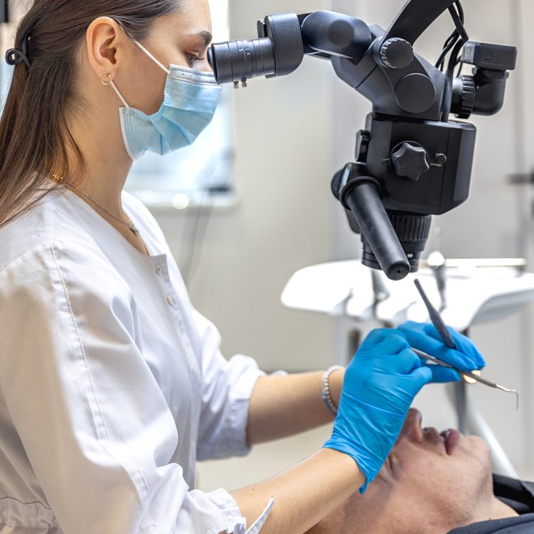 Young female dentist treating patient's teeth with dental microscope. Dentistry concept. High quality photo. Professional dental treatment. Dental equipment.